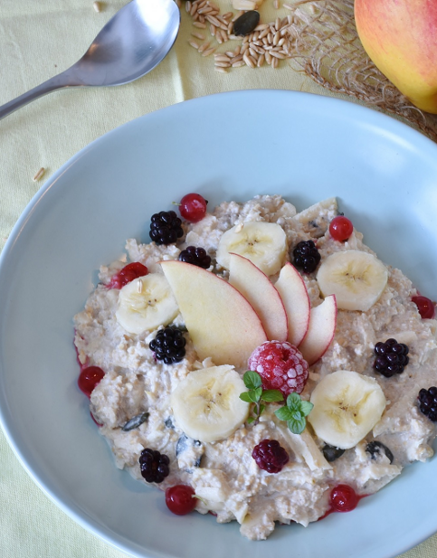 Haferbrei mit Bananen, Apfelscheiben und Beeren in einer blauen Schale, dekoriert mit Minze.